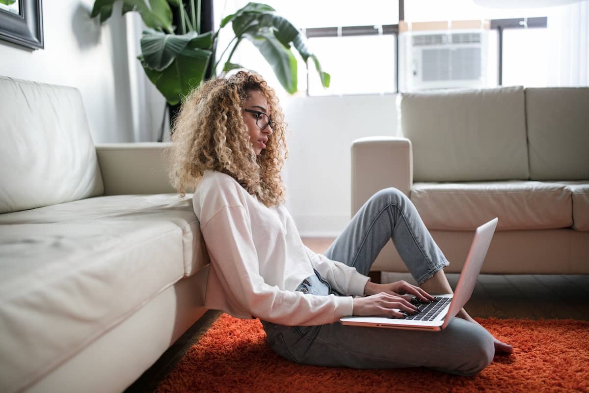 photo of student taking a class live online, seated on their living room floor, leaning against a couch